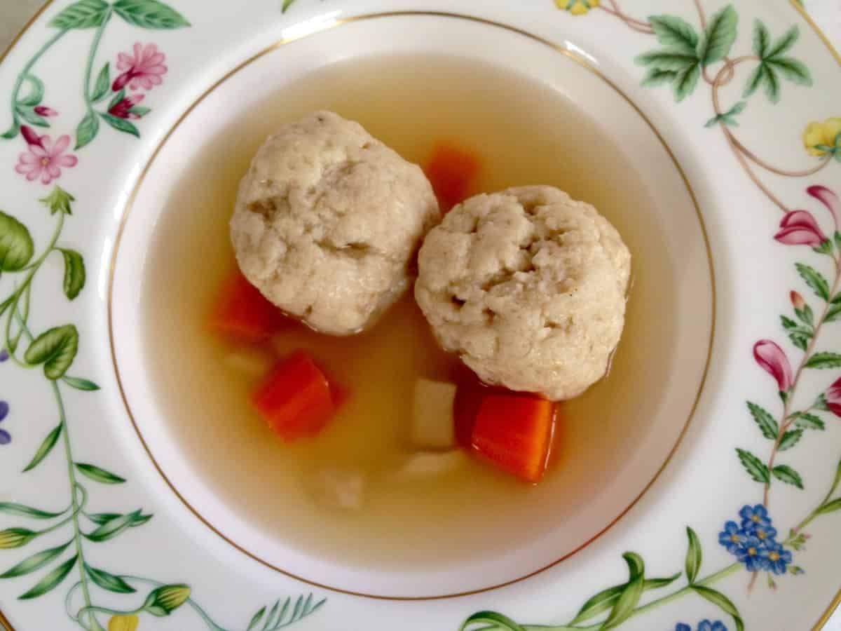 A bowl of matzo ball soup with carrots and chicken.