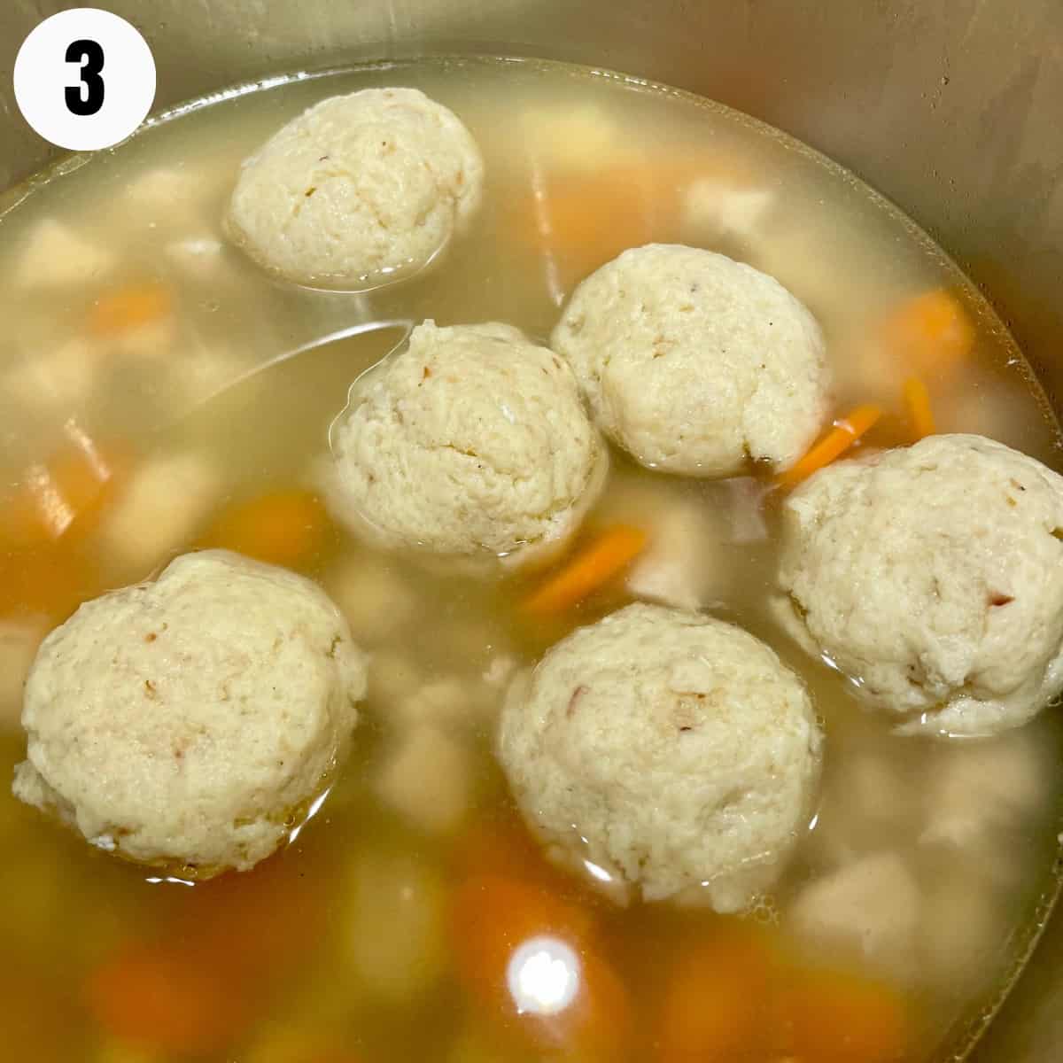 Matzo ball soup in a pot with carrots.