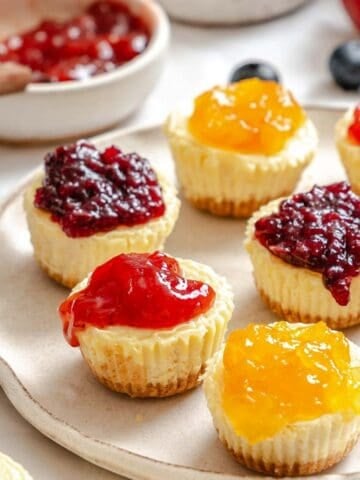 Mini cheesecake bites with various fruit toppings on a plate.
