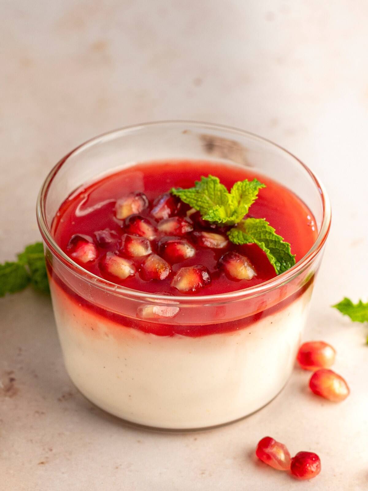 A clear bowl of malabi pudding garnished with pomegranate arils and fresh mint.