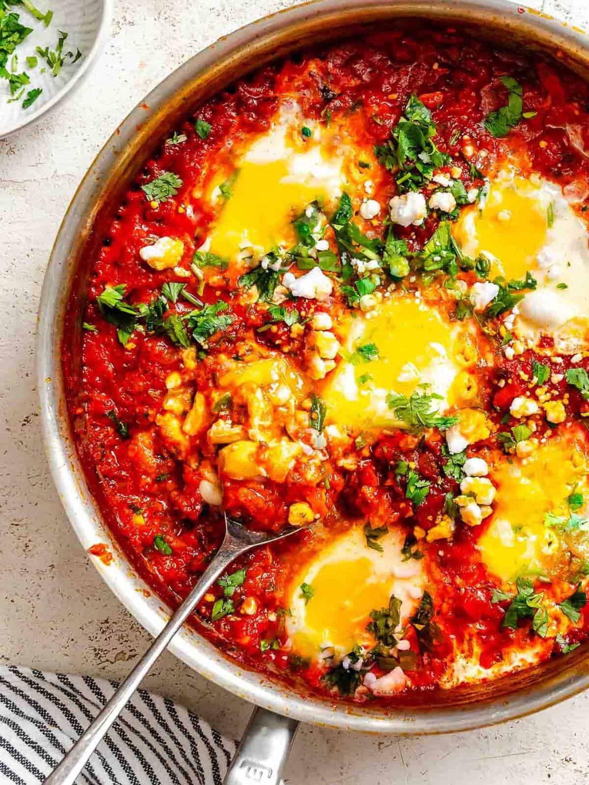 Shakshuka in a pot with a spoon in it.