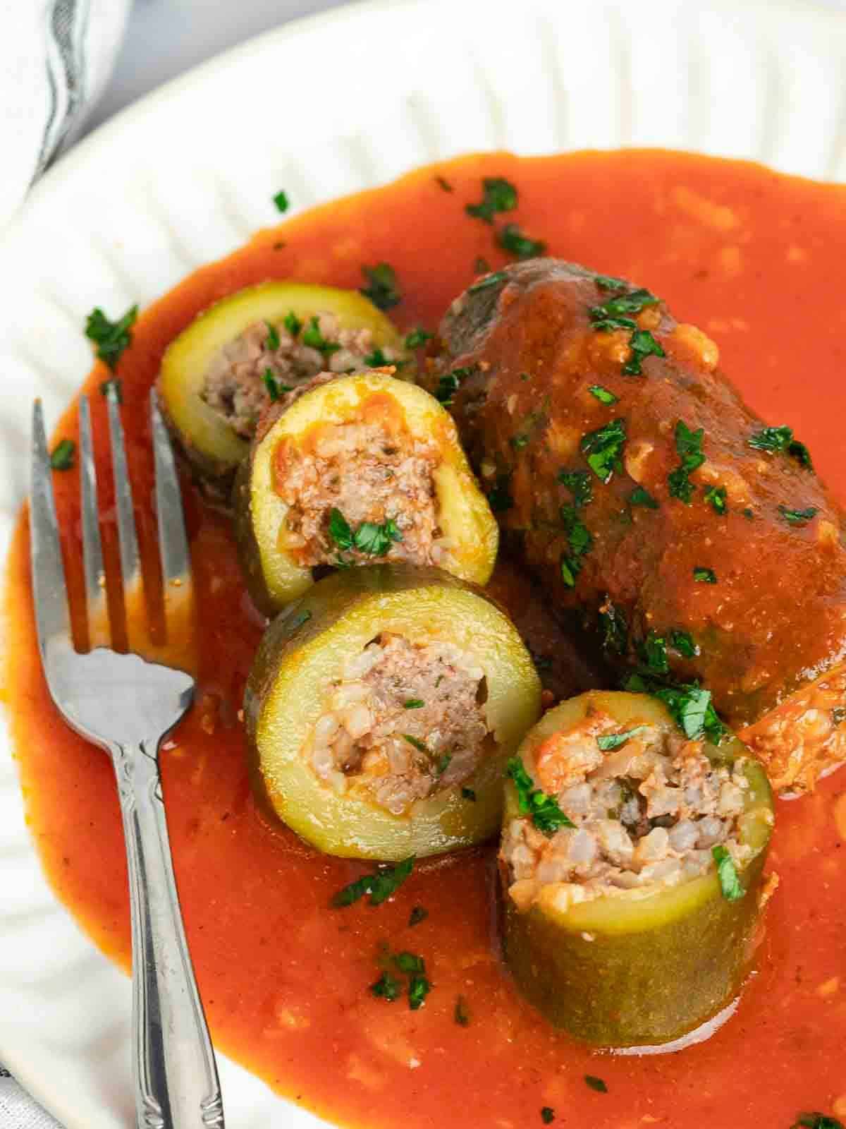 Sliced Kousa Mahshi showing  zucchini is stuffed with meat and rice and topped with tomato sauce. 
