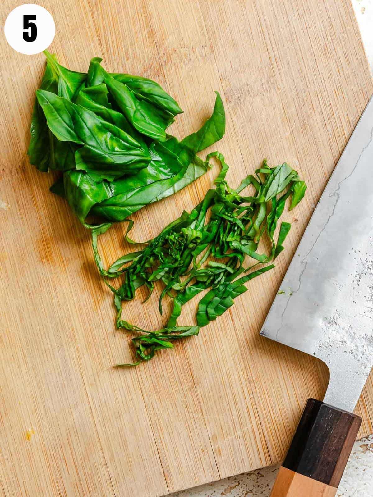 Chopped basil on a wooden cutting board with a knife.