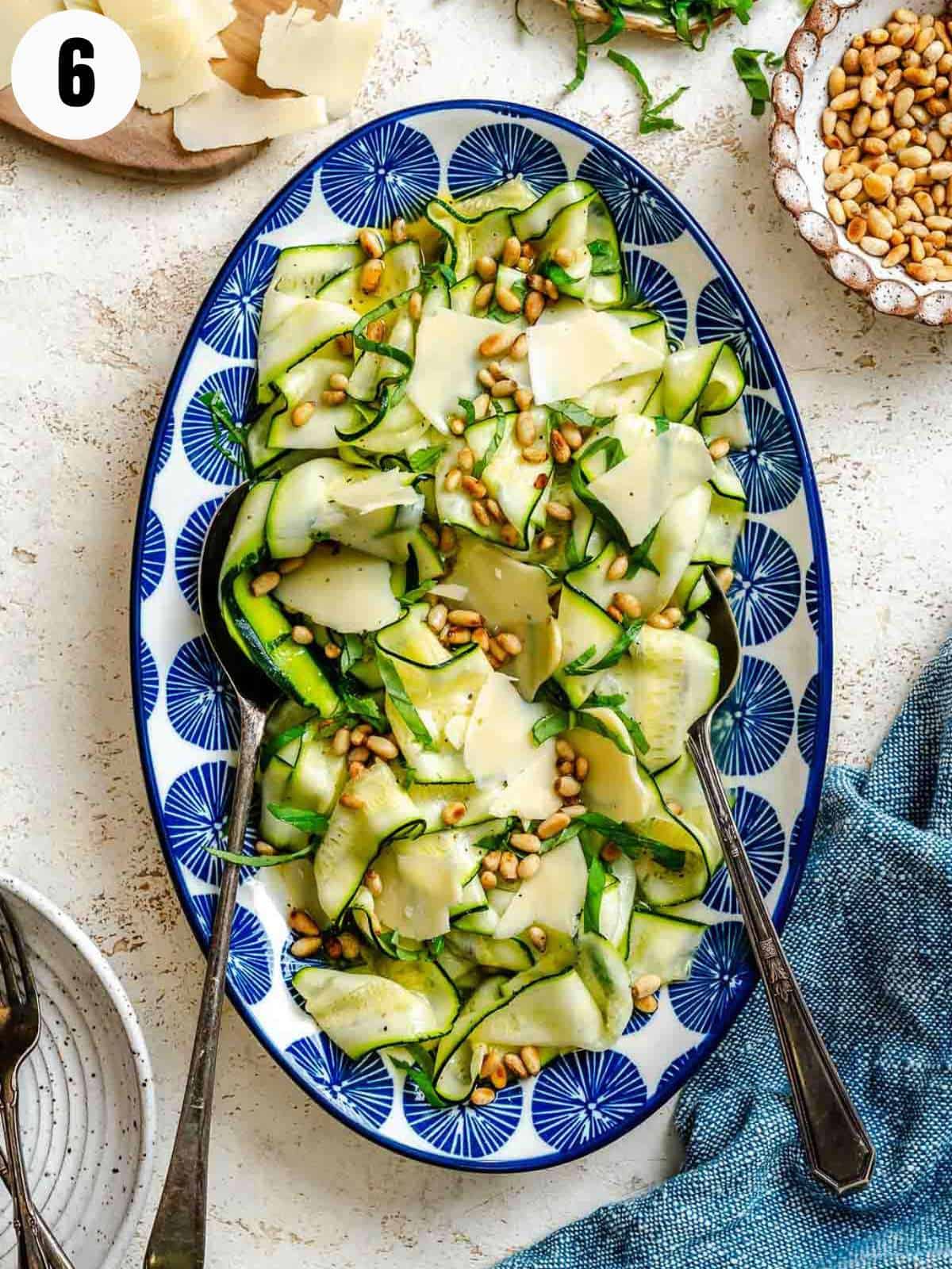 Zucchini ribbon salad with Parmesan shavings and basil on a white and blue serving plate.