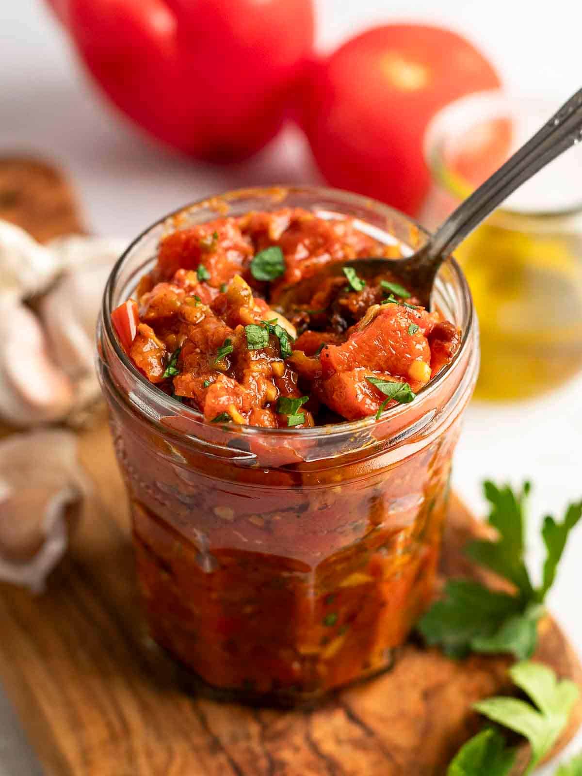 Matbucha in a glass jar with a spoon.
