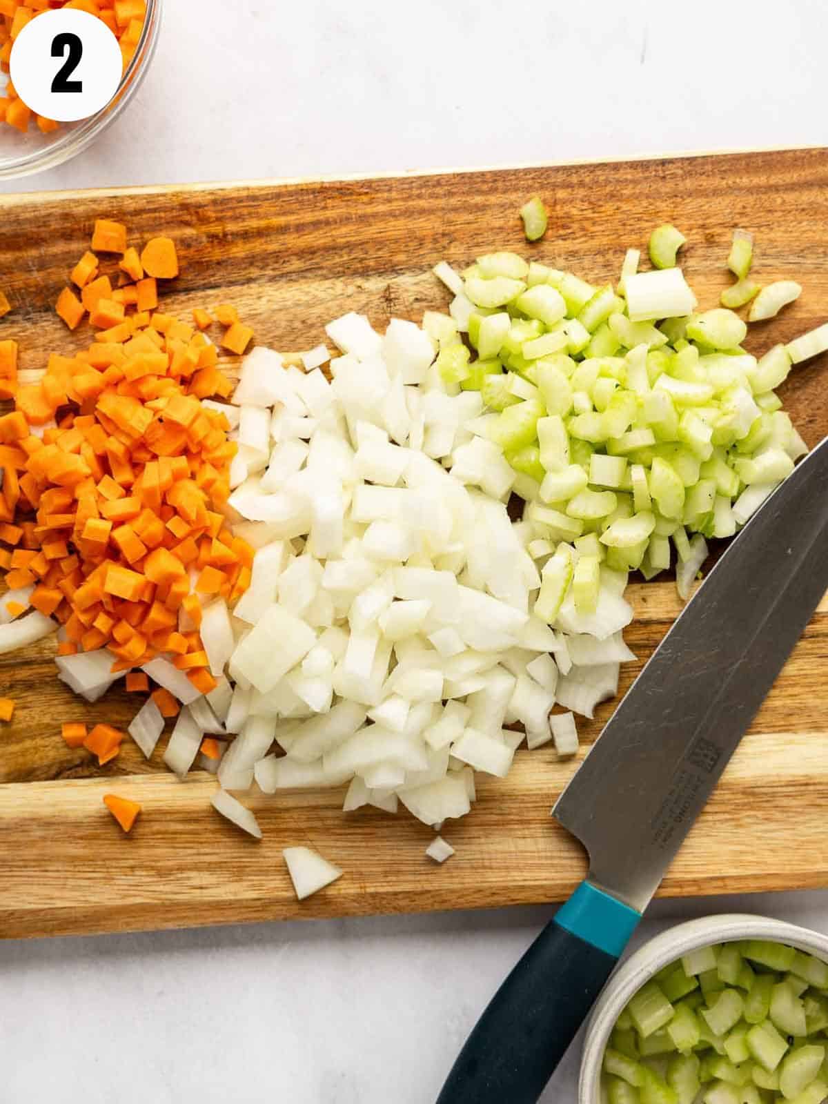 Chopped onions, carrots and celery on a cutting board with a knife.